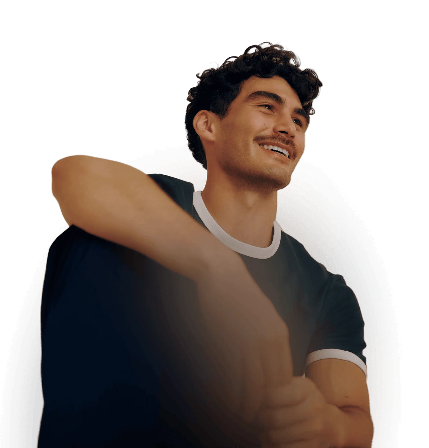A man sitting back relaxed, with his arm on one knee, smiling warmly.